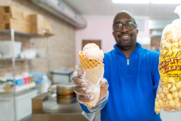 Man reaching over wooden counter holding an ice cream cone and bag of popcorn