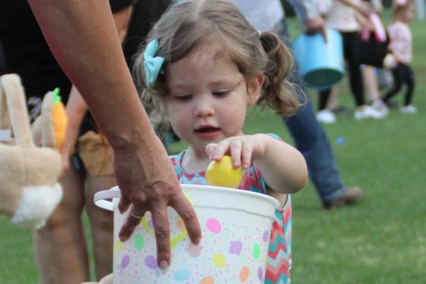 A little girl fills her egg bucket at Pelican Park's Twilight Eggstravaganza egg hunt.