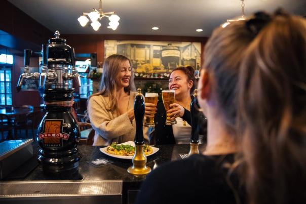 Two people cheering beers at a bar.