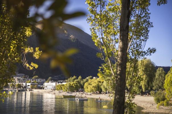 Looking through green trees to big lake, boats, people and buildings