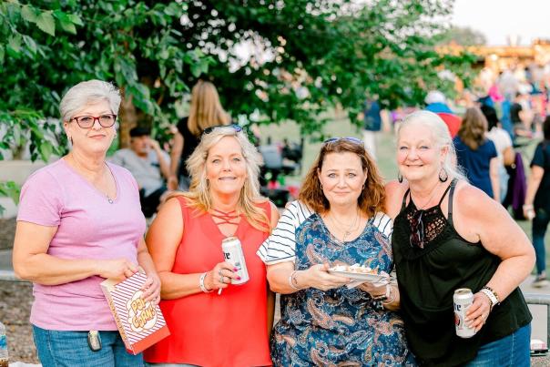 Group of middle aged women, smiling at the camera and holding festival drinks and food