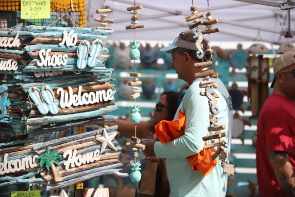 A man browsing a display of hand-crafted, beach-themed wooden signs for sale