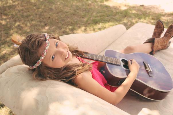 An image of local singer, Abby Stephens, from Johnston County, NC, holding her guitar on a couch.
