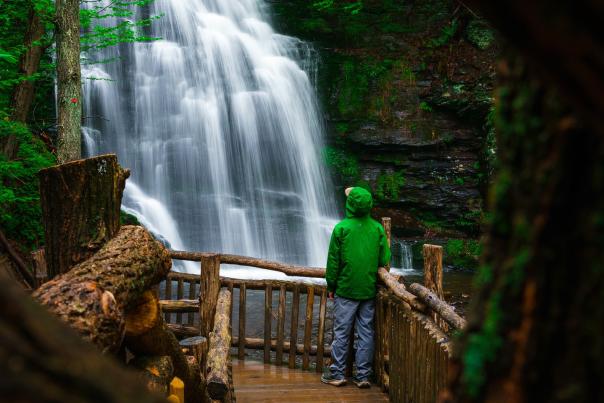 A visitor in a green raincoat looks up at beautiful Bushkill Falls in the Poconos.