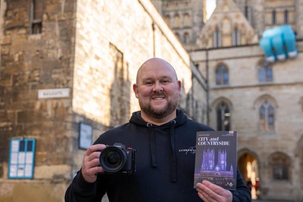 a man smiling holding a Lincoln city guide and a camera