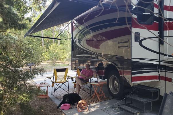 Blonde woman and black dog sit under an RV's awning
