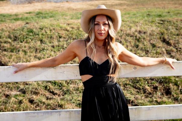 Colbie Caillat posing on a wooden fence wearing a cowboy hat
