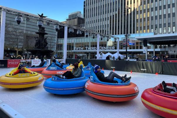 5 ice rink bumper cars colored red, blue, yellow, and orange, holding people who are laughing and bumping the cars into each other on Fountain Square in Cincinnati