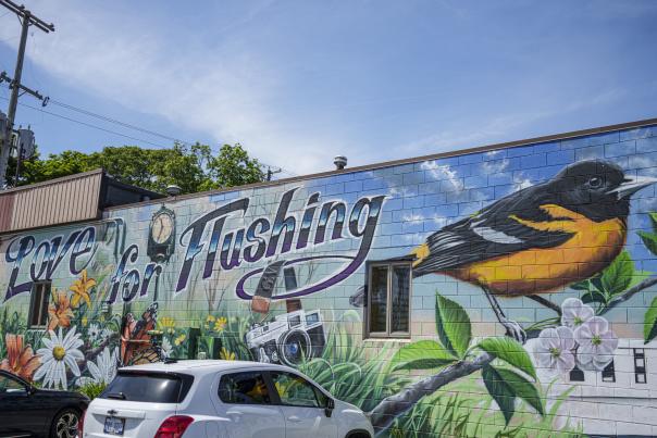 A mural of a yellow and orange bird and flowers decorates the side of a building in Flushing, Michigan.