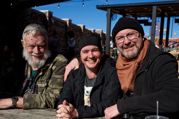 Group of three individuals sitting at a table outside on the patio of Treno Pizzeria. Smiling and drinking sodas as they listen to live music for the monthly Santa Fe Jazz Jam.