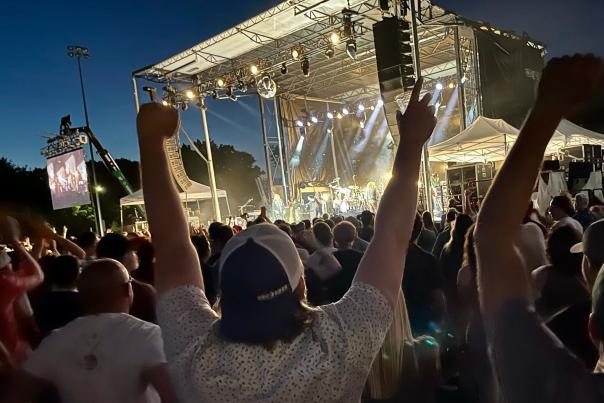 A crowd of people in silhouette wave their arms in the air as they look toward an illuminated stage at Breese Stevens Field.