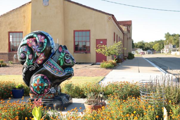 painted black squirrel statue in front of a building surrounded by flowers