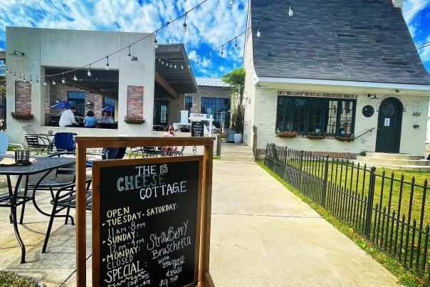 Sidewalk in front of Cheese Cottage with a sign showing hours of operation