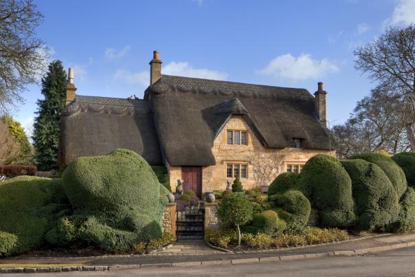 A beautiful thatched cottage surrounded by topiary trees from Manor Cottages in the Cotswolds