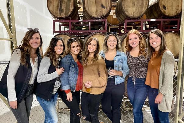 Seven girls posing for a photo in front of barrels at O'so Brewing. Three are holding beer.