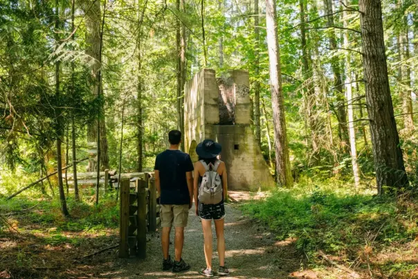 Two people looking at an old broken down building surrounded by forest.
