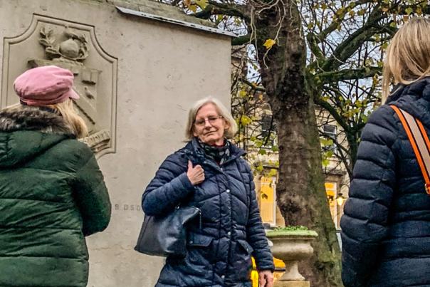 A tour guide stands in front of a monument with three visitors to Cheltenham