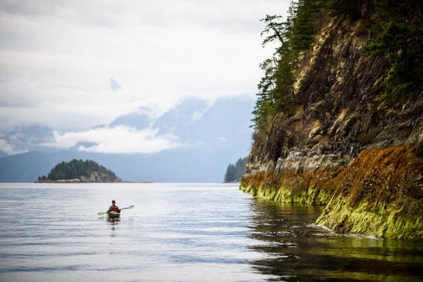 A man kayaks along the rocky coastline.