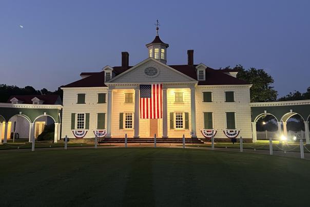 American Village's Washington Hall, a colonial style building painted white, glows with ambient lighting and hangs an American flag from its front porch.