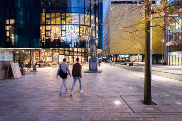 2 people walking in a square in front of HOME venue.