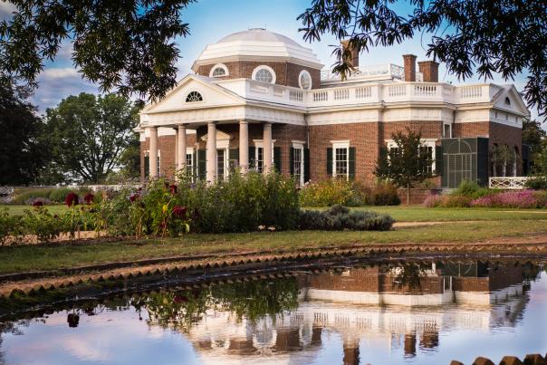 The exterior of Monticello surrounded by folliage, with the reflection of the home showing in a nearby pool