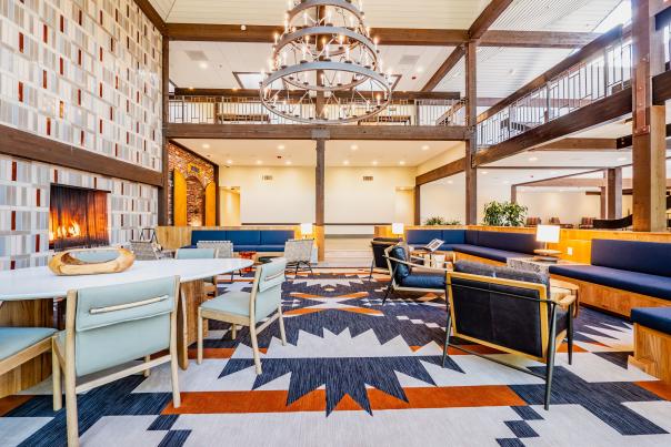 The Valley River Inn lobby showcases a massive chandelier, tiled fireplace and modern seating on a geometric rug.