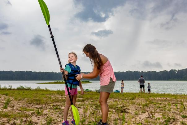 A little girl out of the lake while smiling at her mom at Howell Woods.