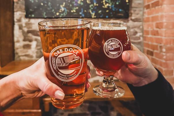 A couple holding beers up in front of MQT sign at Ore Dock Brewing Company