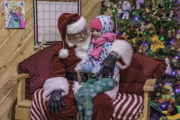 Santa Claus talking with a young child beside a decorated Christmas tree in a cozy, wood-paneled room in Cumberland County, North Carolina.