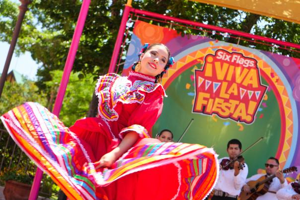 Folklorico dancer in red dress dancing with mariachi band behind her.