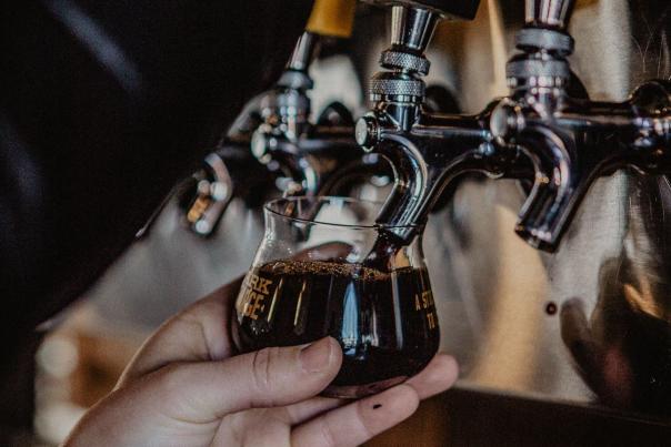 A hand holding a Braxton taster glass up to the craft beer taps for a pour of Dark Charge Imperial Stout in Covington, Ky.