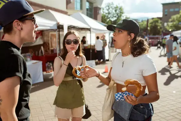 Three friends talking while eating fair food.