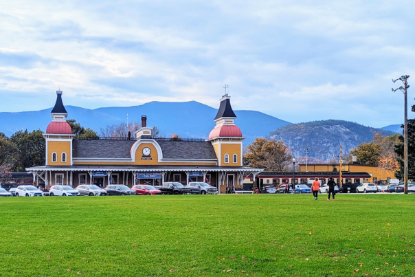 Conway Scenic Railroad Train Station (Exterior, Fall) - Yellow and Orange Train Station with Mountains and Fall Foliage in Background, Grassy Lawn in Foreground