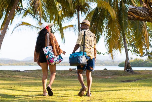 A pair of friends enjoying a leisurely walk along the beach, one holding a bag and the other a cooler.