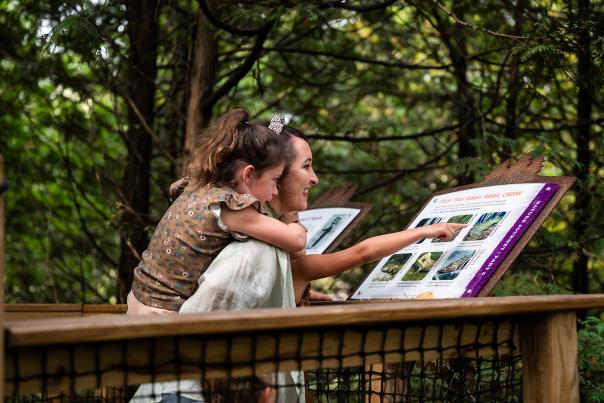 A child rides on her mother's back while reading a sign at the canopy tour at the NEW Zoo and Adventure Park in Green Bay, Wisconsin.