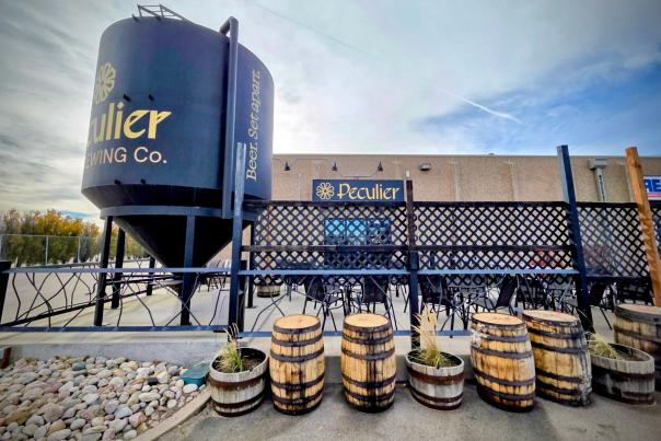 The outside of a brewery with a tank and barrels. The sign says Peculier.