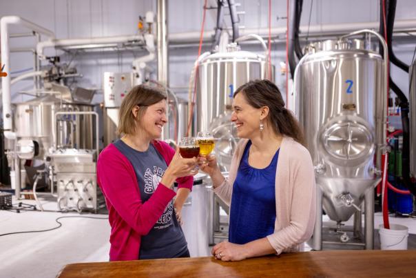 Two women cheers with beer in front of large  brewing tanks at Giant Jones B