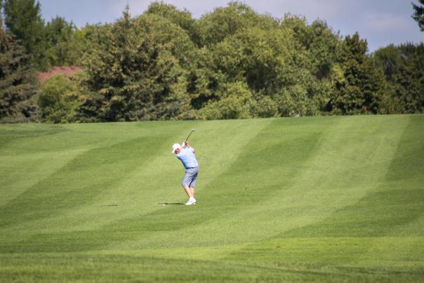man swinging golf club on golf course fairway