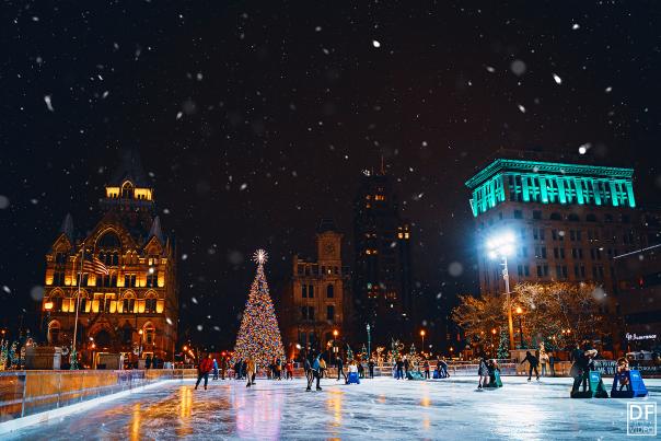 Glowing christmas tree set behind people skating at Clinton Square ice rink at night