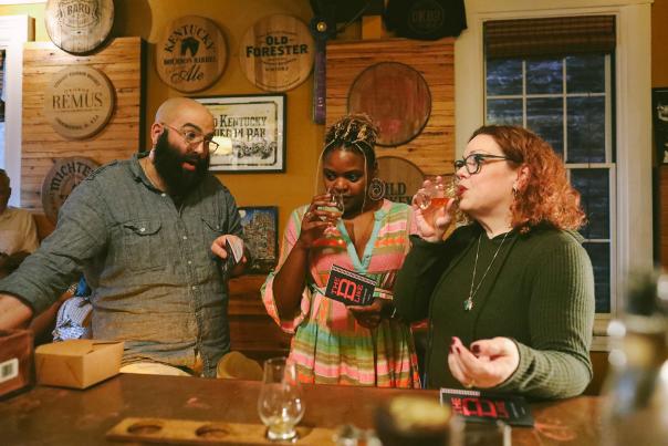 Three people at the bar at Old Kentucky Bourbon Bar. A man chats while two women sniff and sip bourbon.