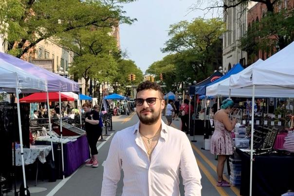 Man walks towards camera with festival tents set up along the street behind him.