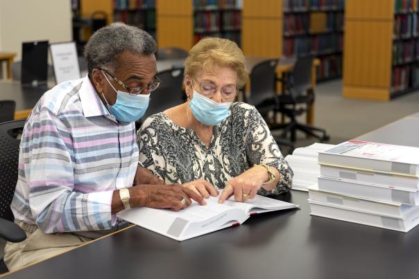Two adults wearing masks looking through index books at the Genealogy Center in Fort Wayne, Indiana