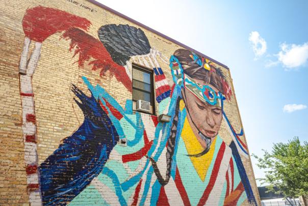 Coming Home mural of Native American women on the side of a tan brick building.