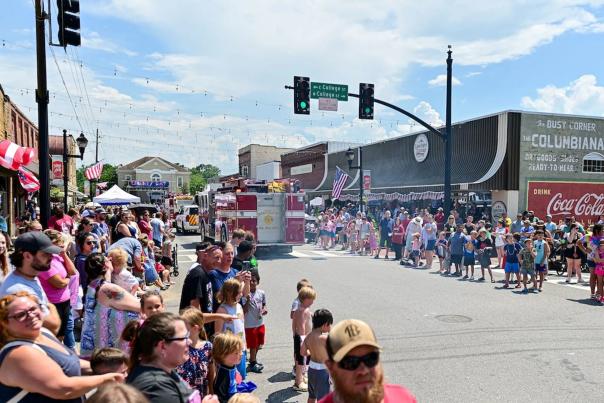 A firetruck drives through the street of downtown Columbiana, surrounded by a large crowd dressed in patriotic gear.