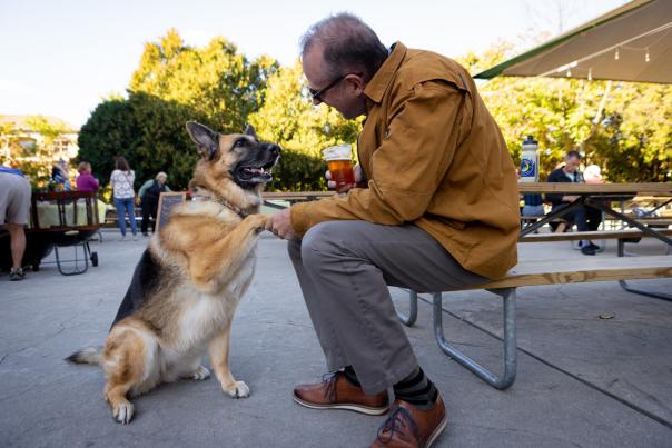 A man shakes paws with a German Shepherd while holding a beer at the Capital Brewery biergarten.