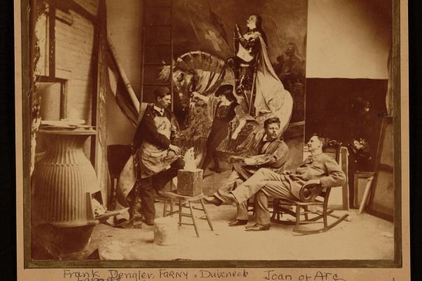 A sepia photo of artists Frank Duveneck and Henry Farny in a studio with a stove and painting of Joan of Arc