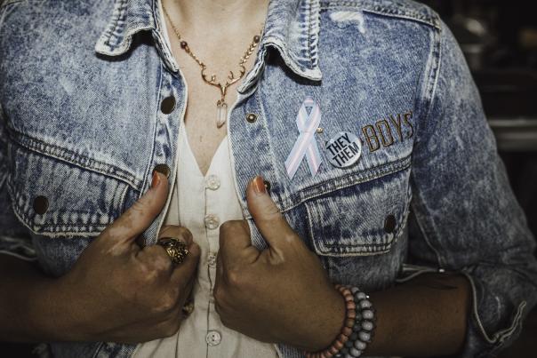 A person wearing a denim jacket with a trans flag ribbion.