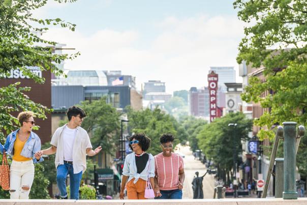 A group of one man and three women walk up the Capitol steps with State Street in the background