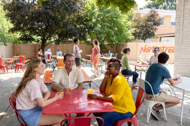 A group of a white man, white woman and Black woman sit on an outdoor patio and drink beer at Northstreet