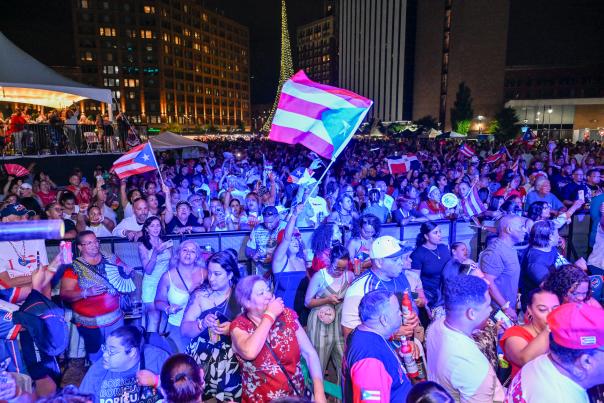 An image of the crowd at the 2024 Rochester Puerto Rican Festival at Parcel 5 in Downtown Rochester. There are two Puerto Rican flags waving in the crowd.